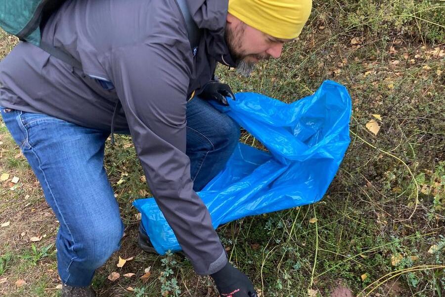 Ein Mann sammelt Müll in einem blauen Sack, er trägt Handschuhe.