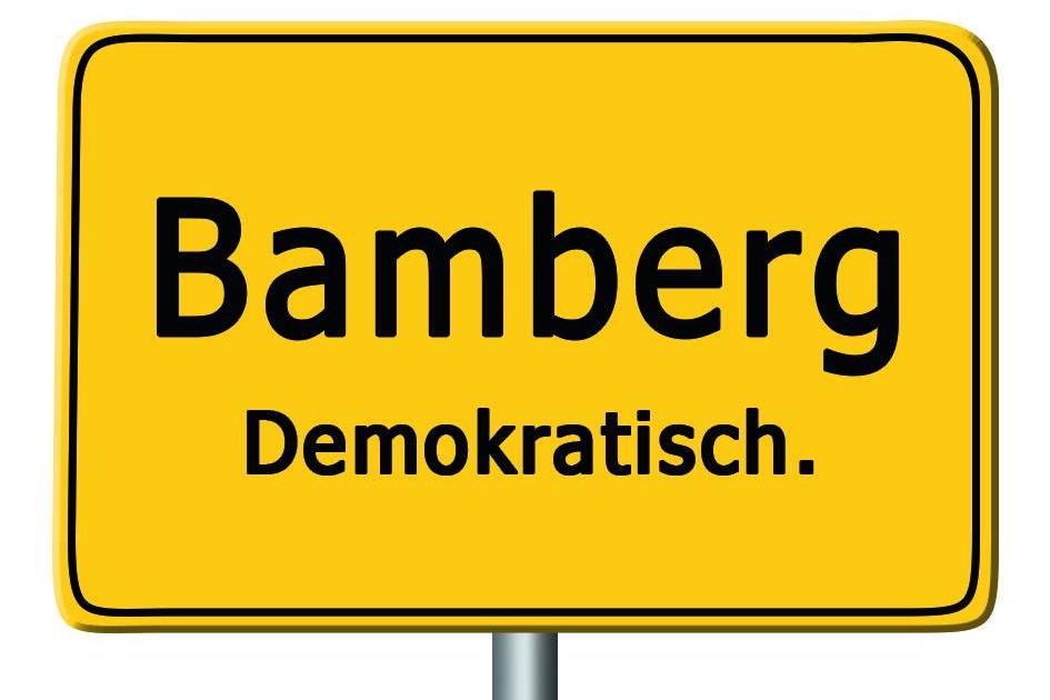 Auf einem gelben Ortsschild steht unter dem Namen der Stadt Bamberg zusätzlich das Wort 'Demokratisch'.