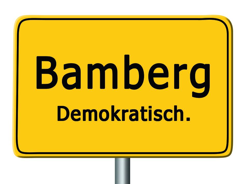 Auf einem gelben Ortsschild steht unter dem Namen der Stadt Bamberg zusätzlich das Wort 'Demokratisch'.